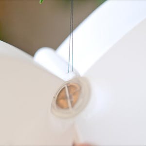 May include: A close-up of a white, butterfly-shaped object, possibly a decorative element or a part of a larger design. The object is suspended by thin, dark strings. The focus is on the object's shape and texture.