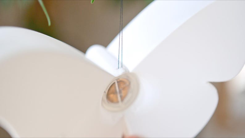 May include: A close-up of a white, butterfly-shaped object, possibly a decorative element or a part of a larger design. The object is suspended by thin, dark strings. The focus is on the object's shape and texture.