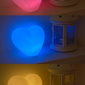 May include: Three heart-shaped lamps, each glowing in a different color: pink, blue, and yellow. The lamps are on a white surface and each is next to a white lantern with a glass window.
