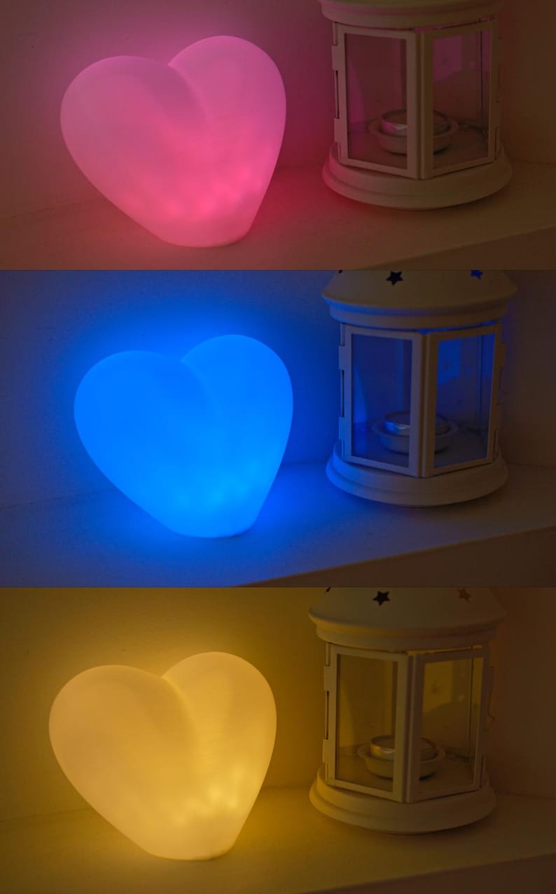 May include: Three heart-shaped lamps, each glowing in a different color: pink, blue, and yellow. The lamps are on a white surface and each is next to a white lantern with a glass window.