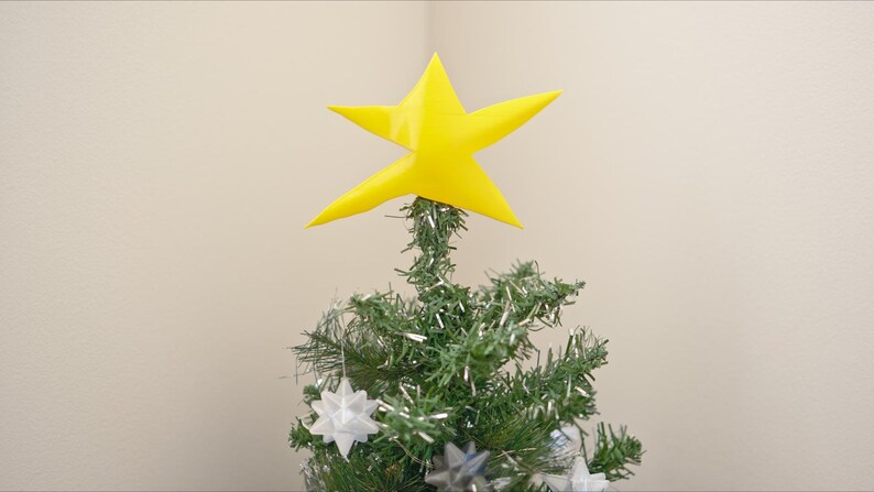 May include: A small artificial Christmas tree decorated with white star ornaments and a yellow star topper.