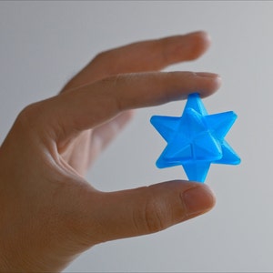 May include: A bright blue, 3D printed, star-shaped object held in a hand.