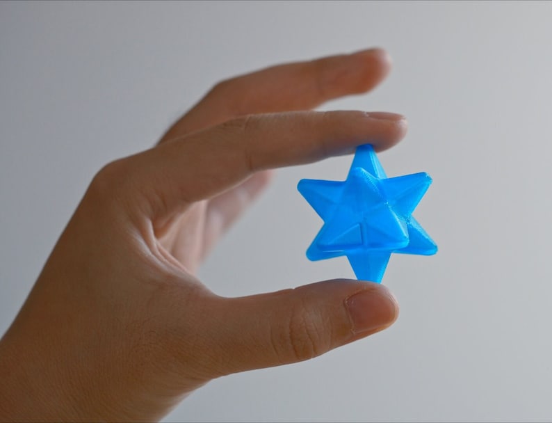 May include: A bright blue, 3D printed, star-shaped object held in a hand.