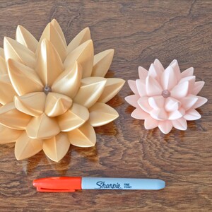 May include: Two decorative lotus flower sculptures, one gold and one pink, on a wooden surface. A red and gray marker is also visible.