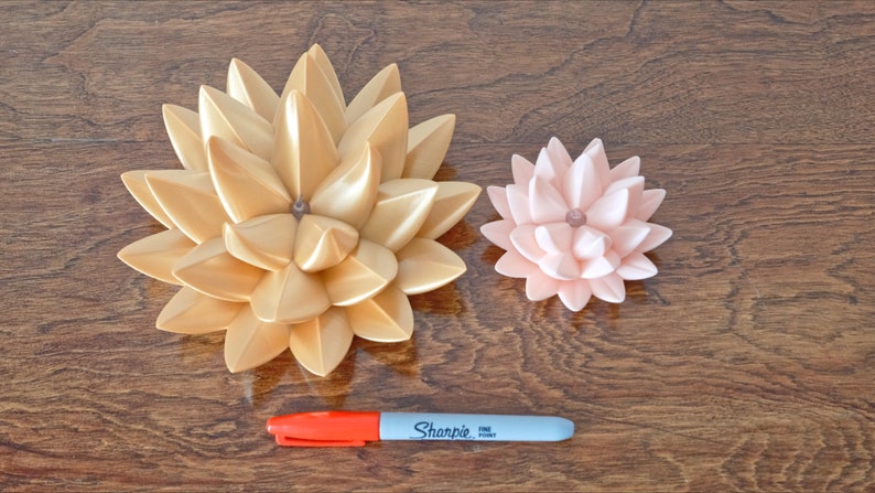 May include: Two decorative lotus flower sculptures, one gold and one pink, on a wooden surface. A red and gray marker is also visible.