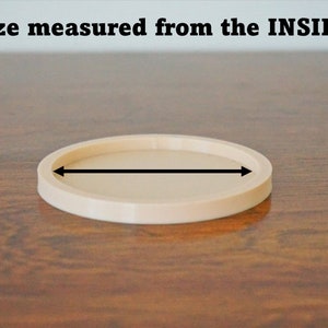 May include: A beige round coaster with a diameter of approximately 4 inches. The coaster is made of a smooth, hard material and has a slightly raised edge.