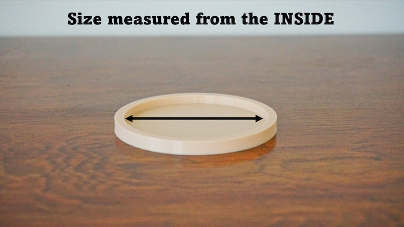 May include: A beige round coaster with a diameter of approximately 4 inches. The coaster is made of a smooth, hard material and has a slightly raised edge.
