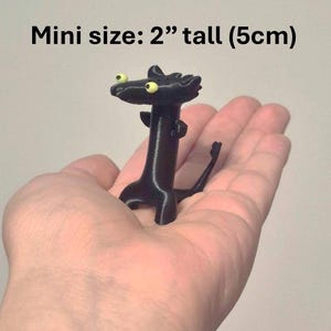 May include: A black, miniature figurine of a creature with yellow eyes, held in a hand. The figurine is 2 inches tall. The text "Mini size: 2" tall (5cm)" is above the figurine.