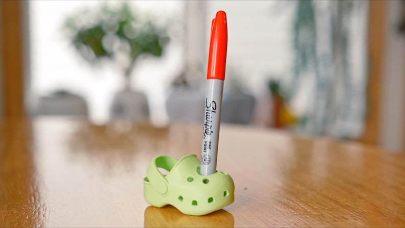May include: A green plastic shoe with a red and grey Sharpie marker inserted into the top opening.