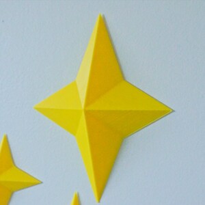 May include: Two yellow paper stars, one large and one small, are attached to a light blue wall.