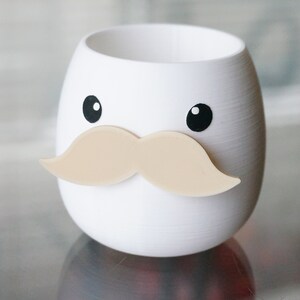 May include: White ceramic planter shaped like an egg with a black mustache and two black eyes.