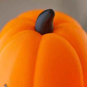 May include: Close-up of the top of an orange plastic pumpkin with a black stem. The pumpkin has a textured surface.