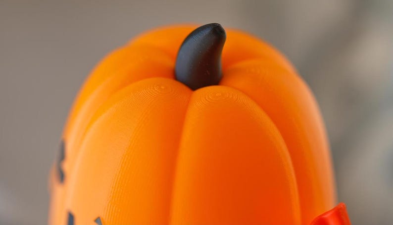 May include: Close-up of the top of an orange plastic pumpkin with a black stem. The pumpkin has a textured surface.