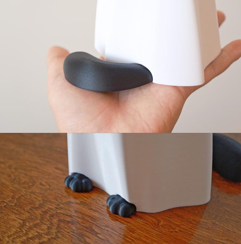May include: White ceramic planter with black cat paw feet. The planter has a rounded shape and a smooth surface. The cat paw feet are made of a soft, flexible material.
