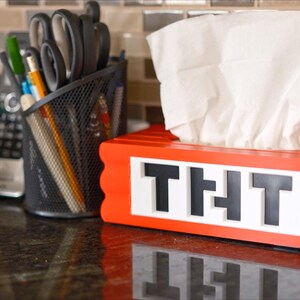 May include: Red tissue box holder with the word "THT" in black letters. The holder is made to look like a stack of red building blocks.