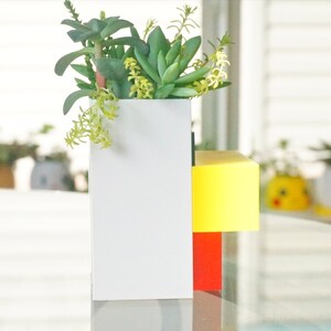 May include: A white planter with a yellow and red base, filled with green and yellow succulents.