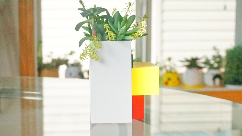 May include: A white planter with a yellow and red base, filled with green and yellow succulents.