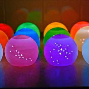May include: A collection of glowing, spherical lamps in various colors, each displaying a constellation pattern. The lamps are in shades of blue, pink, purple, green, orange, and yellow, creating a vibrant and colorful display.