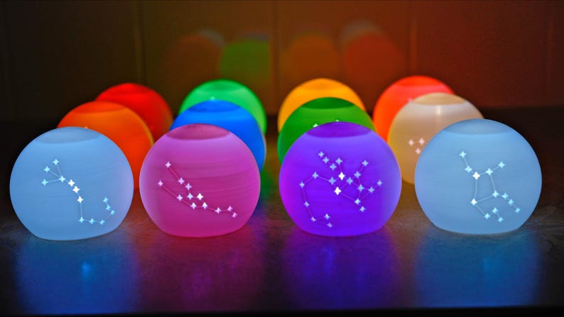 May include: A collection of glowing, spherical lamps in various colors, each displaying a constellation pattern. The lamps are in shades of blue, pink, purple, green, orange, and yellow, creating a vibrant and colorful display.