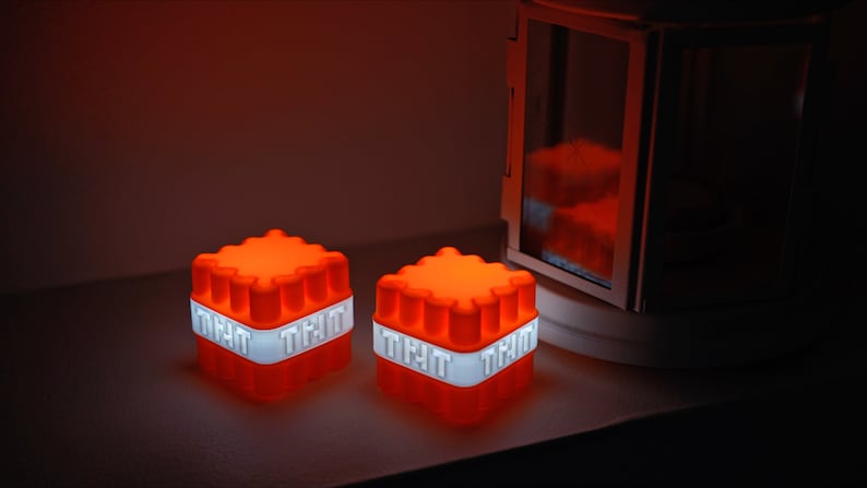 Op de afbeelding: Twee oranje en witte lichtgevende TNT-blokken met het woord "TNT" gedrukt op elke zijde.
