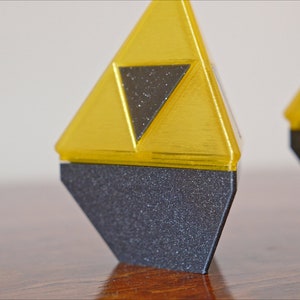 May include: Two golden triangular figurines with a black triangular design in the center. The figurines are standing on a black base.