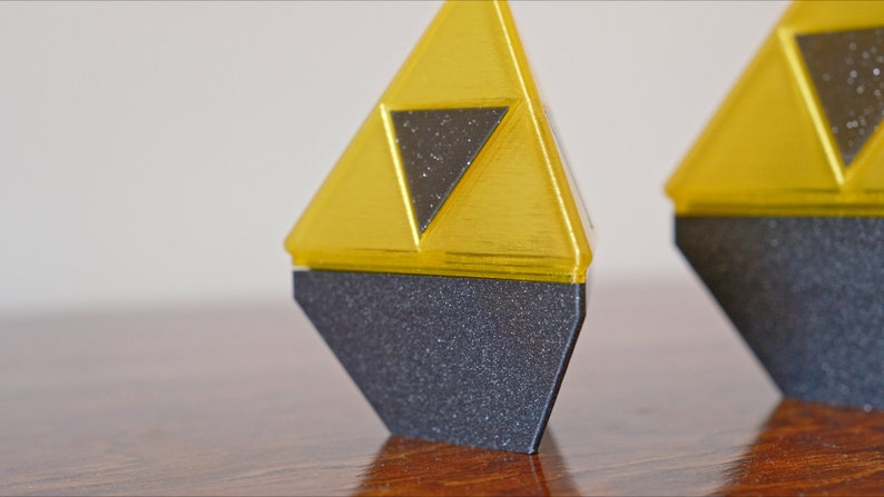 May include: Two golden triangular figurines with a black triangular design in the center. The figurines are standing on a black base.