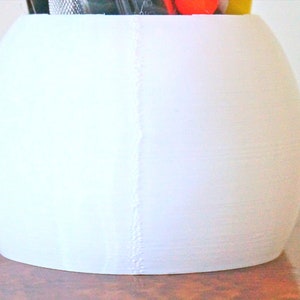 May include: White ceramic desk organizer shaped like a sphere with a seam down the side.