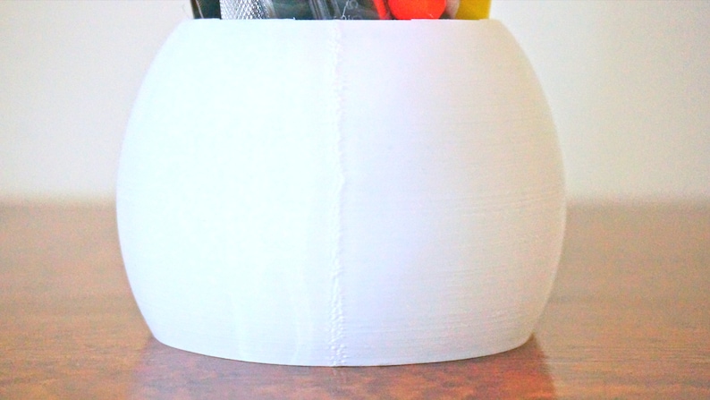 May include: White ceramic desk organizer shaped like a sphere with a seam down the side.