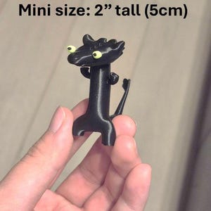 May include: A black figurine of a dragon-like creature, 2 inches tall, with large yellow eyes. The figure has a long neck, small arms, and a tail. The text "Mini size: 2" tall (5cm)" is above the figure.