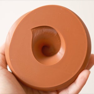 May include: A terracotta-colored silicone mold with a swirl design. The mold is shaped like a donut with a hole in the center.