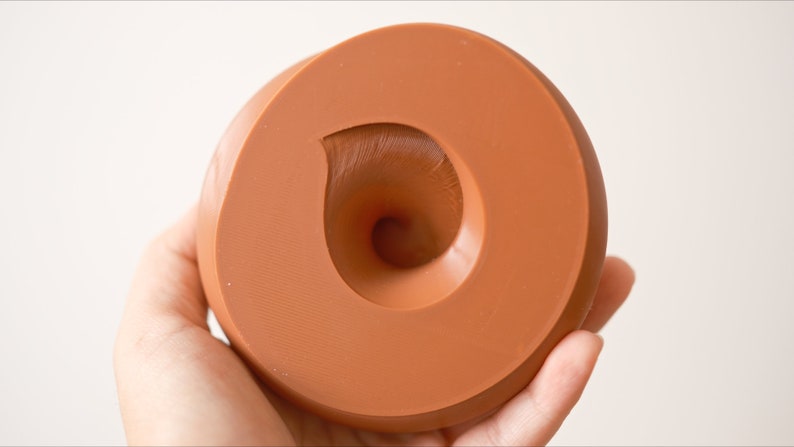 May include: A terracotta-colored silicone mold with a swirl design. The mold is shaped like a donut with a hole in the center.