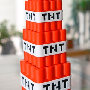 May include: A stack of four red plastic blocks with the word "TNT" printed in black on each block. The blocks are stacked on top of each other, with the largest block on the bottom and the smallest block on top.