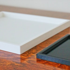 May include: Two square trays, one white and one black, on a wooden surface.