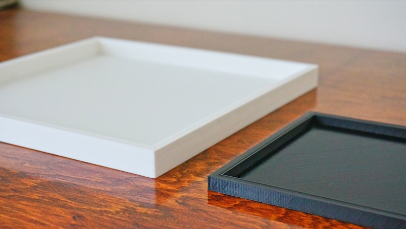 May include: Two square trays, one white and one black, on a wooden surface.