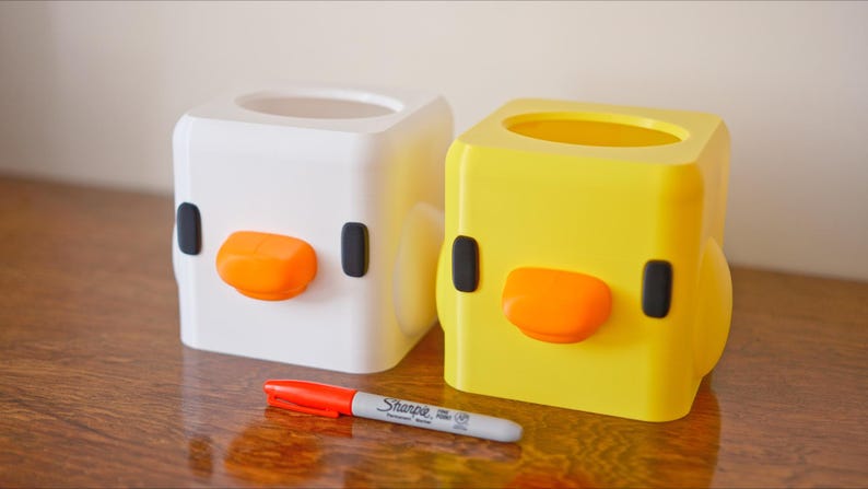 Pu&ograve; includere: Due coperture quadrate per scatola di fazzoletti, una bianca e una gialla, a forma di pulcino dei cartoni animati con occhi neri e becco arancione.