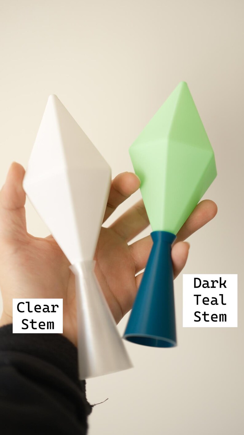 May include: Two geometric-shaped objects are held in a hand. One is white with a clear stem, and the other is green with a dark teal stem. The text "Clear Stem" and "Dark Teal Stem" are visible.