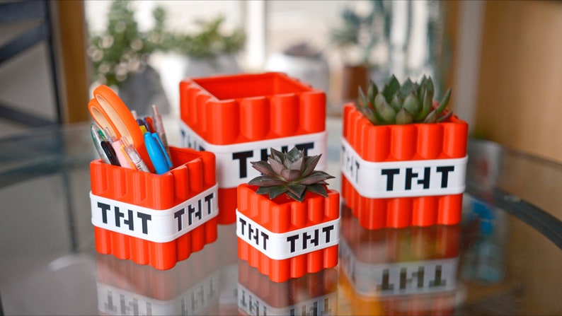 May include: Four red and white Minecraft TNT-themed containers. Two are filled with pens and pencils, and two are filled with small green succulents.