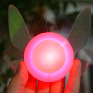 May include: A glowing red light with a translucent, white, wing-like design on either side. The light is held in a person's hand.