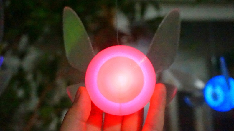 May include: A glowing red light with a translucent, white, wing-like design on either side. The light is held in a person's hand.