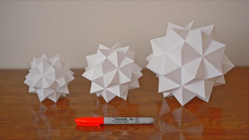 Pode incluir: Tr&ecirc;s formas geom&eacute;tricas de papel branco de tamanhos diferentes. As formas s&atilde;o todas feitas de papel dobrado e t&ecirc;m um design de estrela. As formas est&atilde;o dispostas em uma fila da menor para a maior.