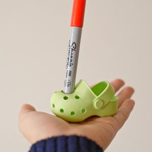 May include: A green plastic shoe with a red and white Sharpie marker sticking out of the top.