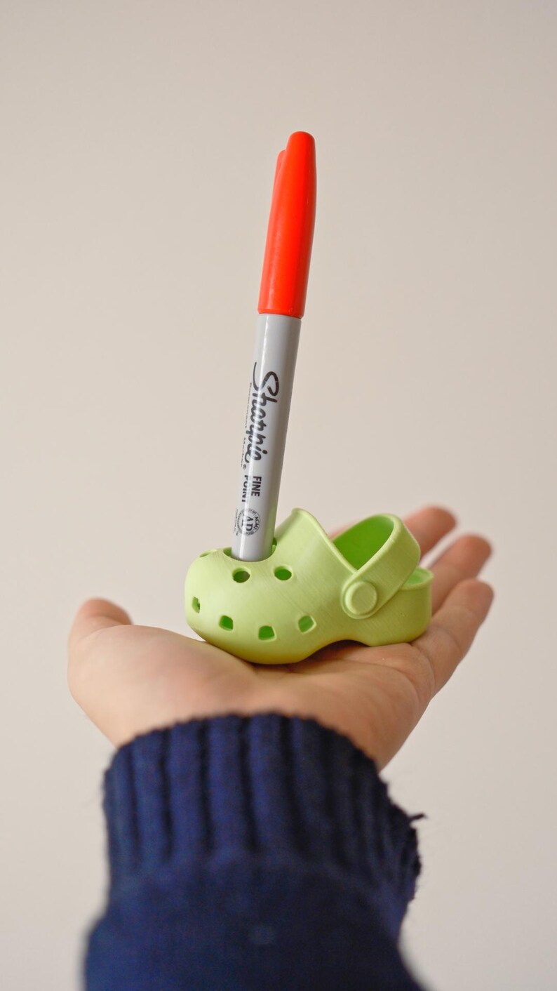 May include: A green plastic shoe with a red and white Sharpie marker sticking out of the top.