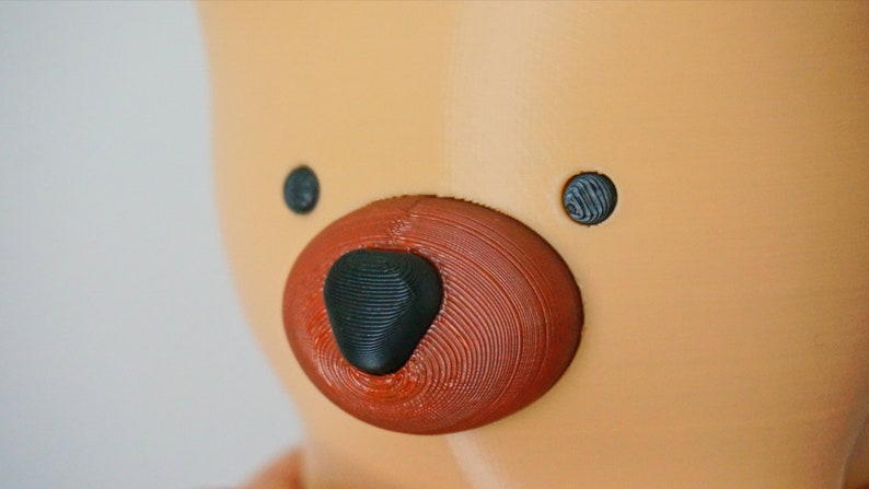 Puede incluir: Primer plano de la cara de un oso de peluche marr&oacute;n con ojos negros y una nariz roja.