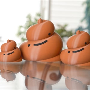 May include: Three brown ceramic figurines shaped like poop with smiling faces. The figurines are different sizes and are arranged in a row on a glass surface.
