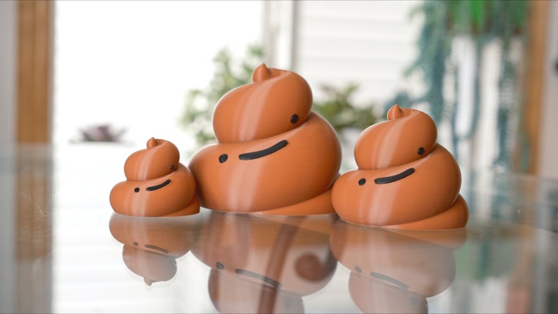 May include: Three brown ceramic figurines shaped like poop with smiling faces. The figurines are different sizes and are arranged in a row on a glass surface.