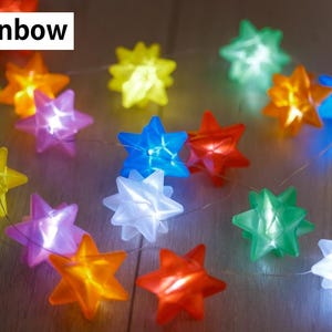 May include: A string of colorful star-shaped lights in various colors, including blue, green, yellow, orange, red, and purple. The lights are strung together on a thin wire. The text "Clear Rainbow" is in the top left corner.