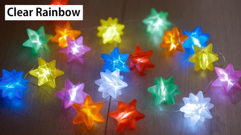 May include: A string of colorful star-shaped lights in various colors, including blue, green, yellow, orange, red, and purple. The lights are strung together on a thin wire. The text "Clear Rainbow" is in the top left corner.