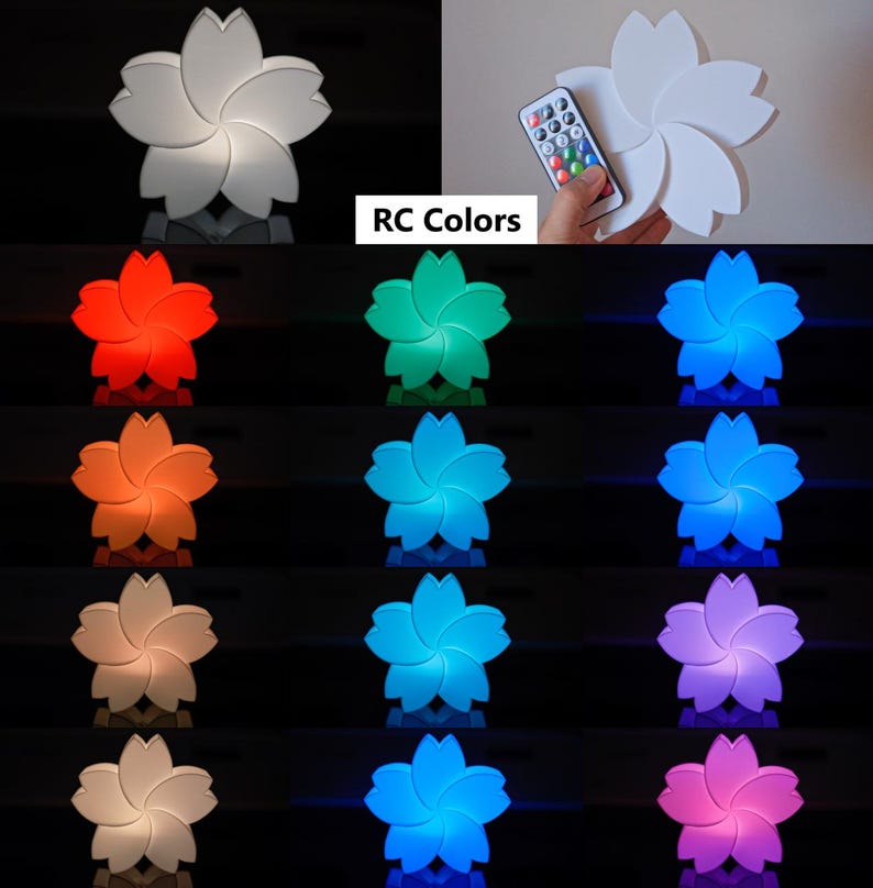 Puede incluir: Una luz nocturna blanca en forma de flor de cinco p&eacute;talos con un mando a distancia. La luz se puede cambiar a diferentes colores, incluidos rojo, naranja, amarillo, verde, azul, morado y rosa. "RC Colors" est&aacute; escrito en la imagen.