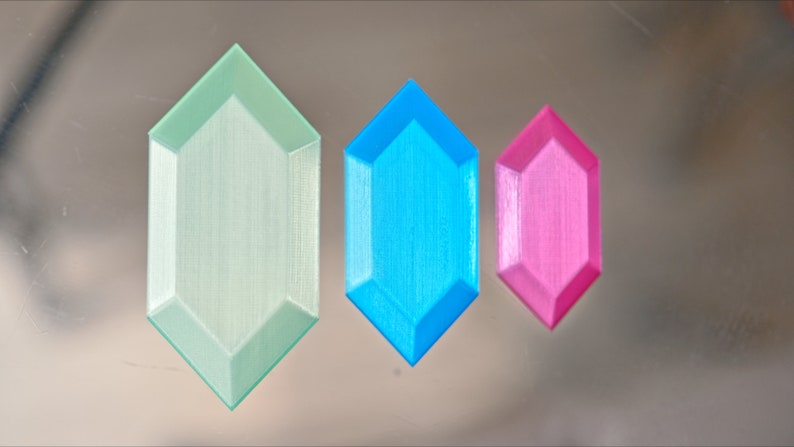 May include: Three 3D printed octagonal gems in different sizes. The largest gem is light green, the middle gem is light blue, and the smallest gem is pink.