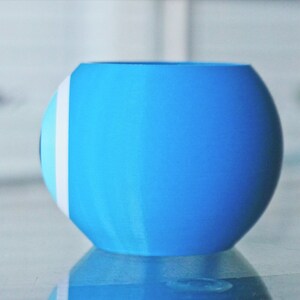 May include: A light blue ceramic planter with a white and light blue design. The planter is round and has a smooth surface.